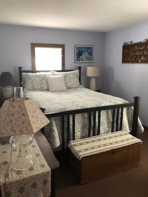 Quarto com cama, mesas de cabeceira, abajur, um banco de madeira e prateleira fixada na parede.