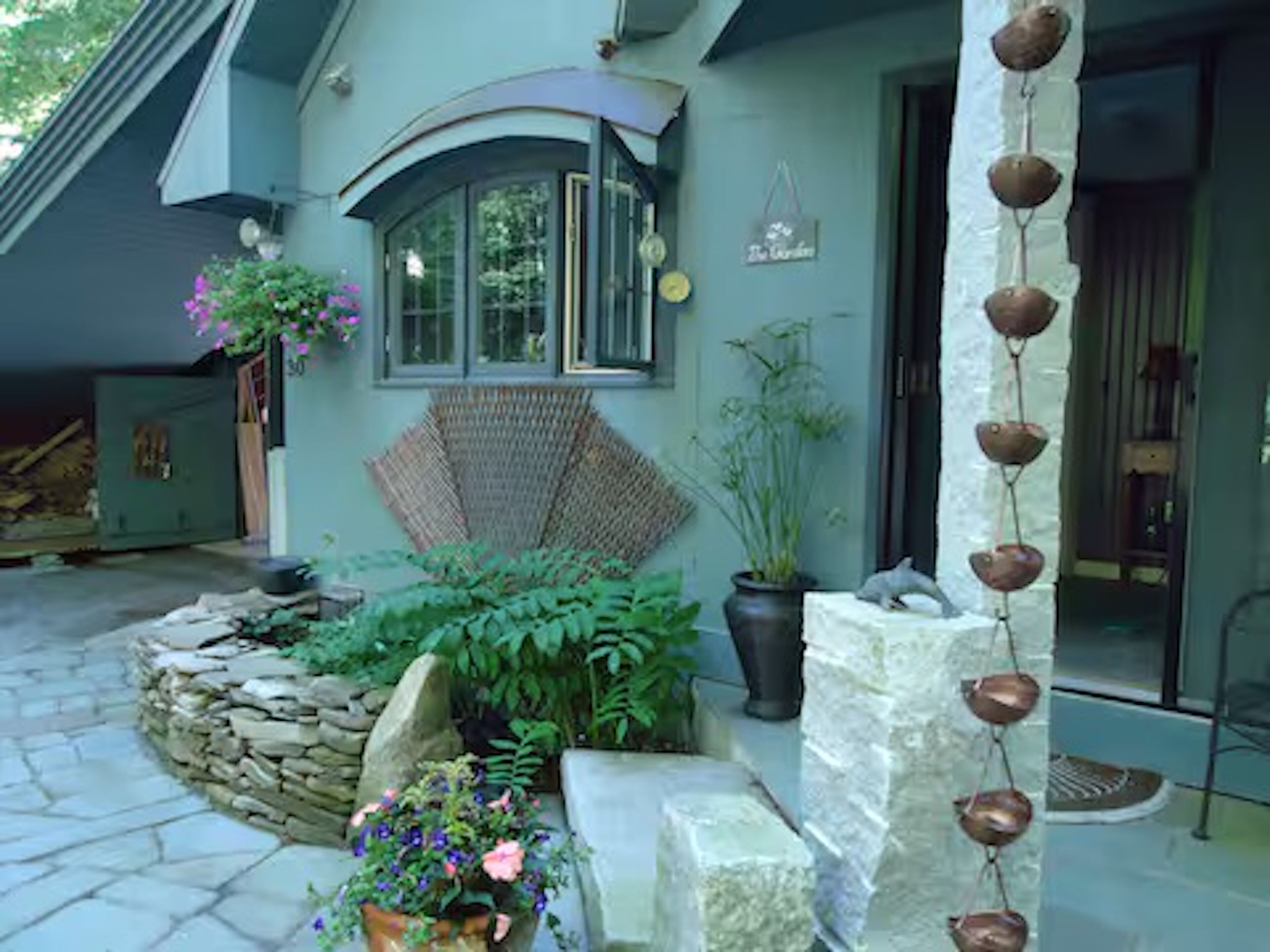 A stone pathway leading to a house with a covered porch area, potted plants, and a hanging decoration.