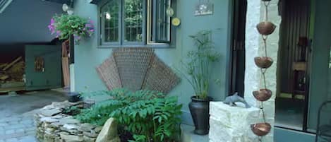 A stone pathway leading to a house with a covered porch area, potted plants, and a hanging decoration.