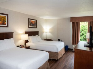 A hotel room with two beds, a desk, a TV, and a window with curtains. - Timmins Inn & Suites (Timmins)