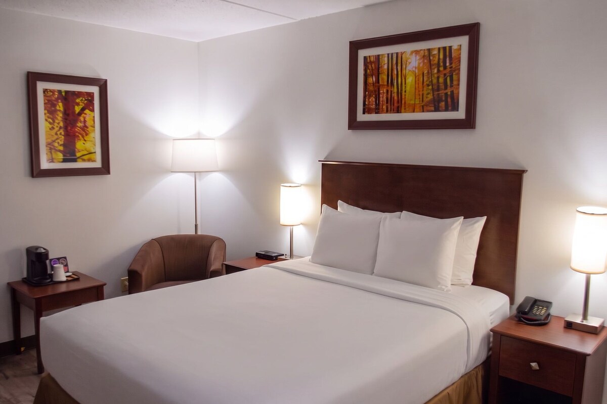 A hotel room with a large bed, two bedside tables, a chair, and two wall-mounted lamps.