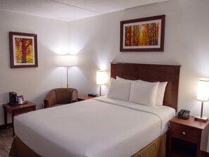 A hotel room with a large bed, two bedside tables, a chair, and two wall-mounted lamps. - Timmins Inn & Suites (Timmins)