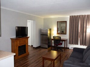 A living room with a television, a fireplace, a refrigerator, a dining table with a chair, and a couch. - Timmins Inn & Suites (Timmins)