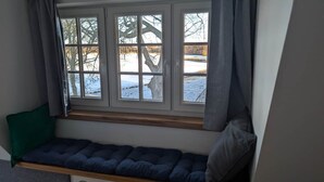 Ikkunan vieressä oleva istuin, jossa on pehmuste, ja ikkunasta avautuu lumisen maiseman näkymä sekä näkyy puu ulkona.