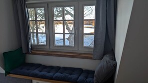 Asiento junto a la ventana con un cojín, vista a un paisaje nevado y un árbol afuera.