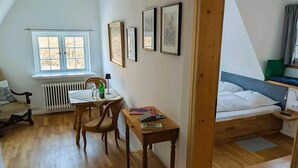 Huoneessa on sänky, pöytä, tuoleja, patteri ja seinällä on kehystettyjä kuvia.