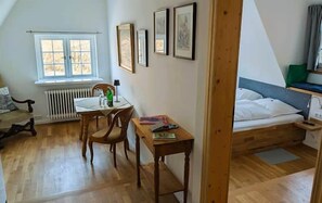 Una habitación con cama, una mesa, sillas, un radiador y cuadros en la pared.