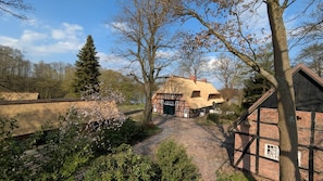 A traditional half-timbered house with a thatched roof, a stone pathway, and a garden with flowering plants.