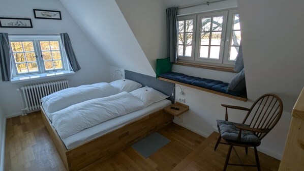 A bedroom with a bed, a chair, a window with a view, and a radiator.
