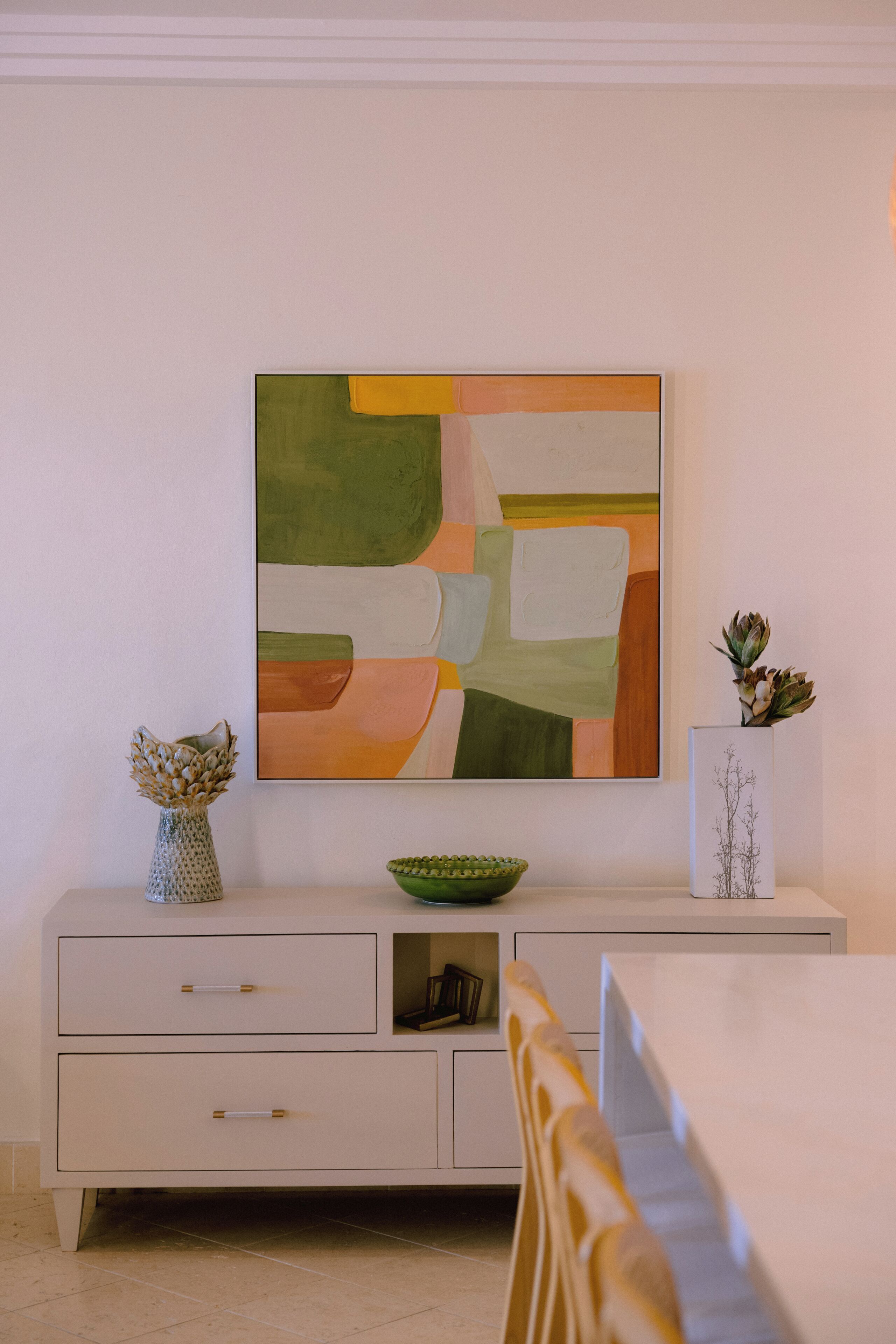 Een modern interieur met een minimalistische witte kast, een groene kom en een ingelijste botanische print.