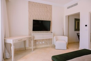 A room with a flat-screen TV mounted on a wall, a white desk, a white armchair, and a green bench. - Marina View 2-Bedroom Apartment | Fishing Lodge Cap Cana (Punta Cana)