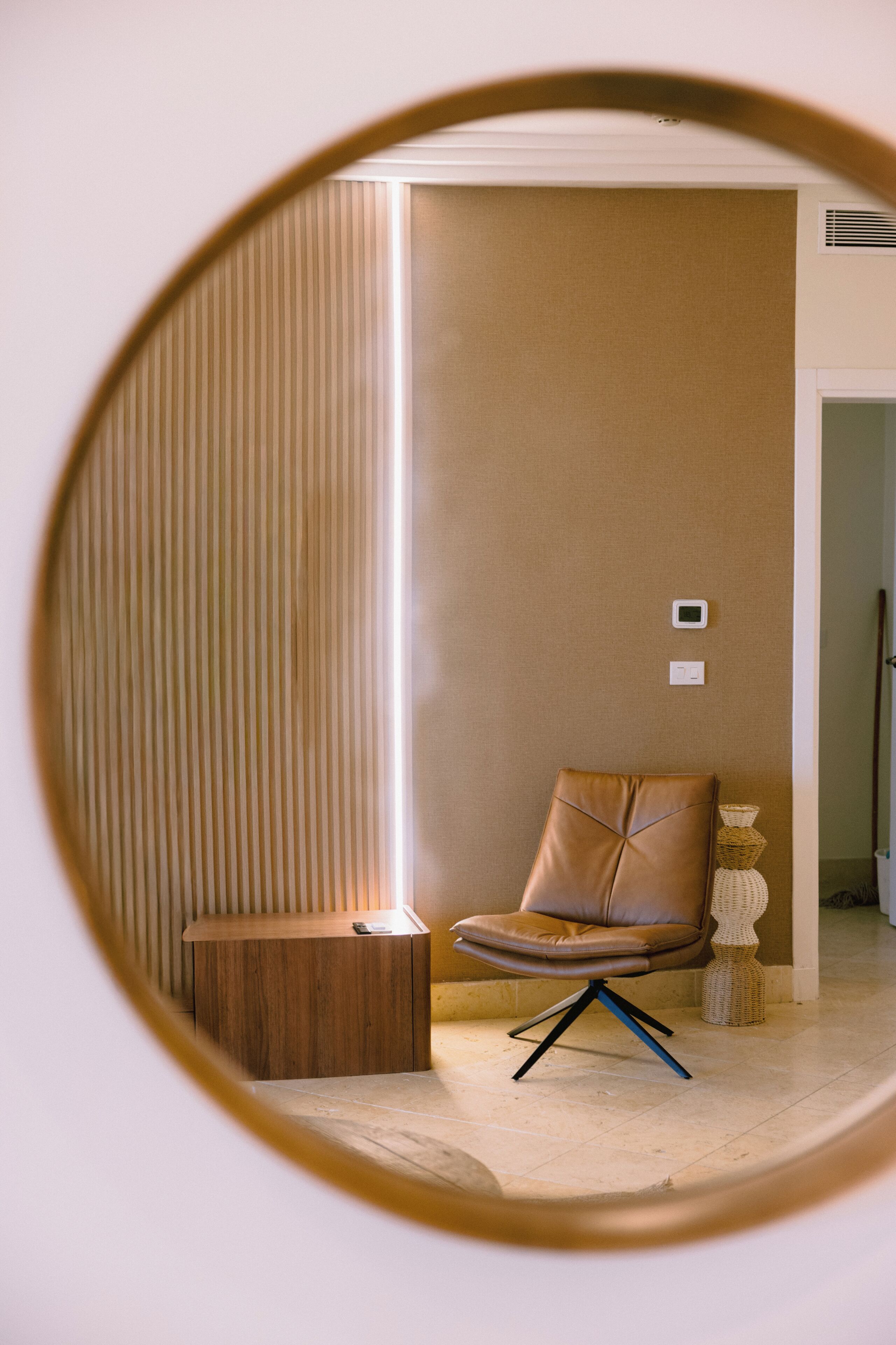 A room with a brown leather chair, a wooden side table, and a woven floor lamp.