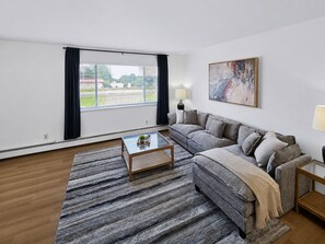 Ein modernes Wohnzimmer mit großem Fenster, einer Couch, einem Couchtisch und einem Bild an der Wand.