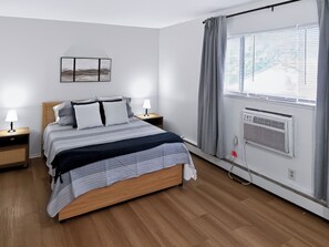 A bedroom with a bed, bedside lamps, a wall-mounted air conditioner, and a window with blinds. - Modern Traditional #10 + 2nd floor + 1 Bed/1 Bath (Lansing)
