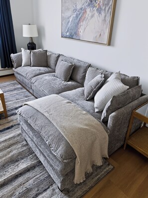 A grey sectional sofa with multiple cushions, a white throw blanket, and a wooden coffee table. - Modern Traditional #10 + 2nd floor + 1 Bed/1 Bath (Lansing)