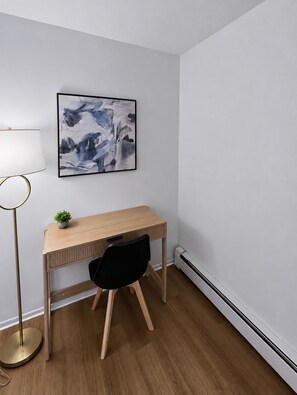 Ein Zimmer mit einem Holztisch, einem schwarzen Stuhl, einer Stehlampe und einem an der Wand hängenden abstrakten Gemälde.