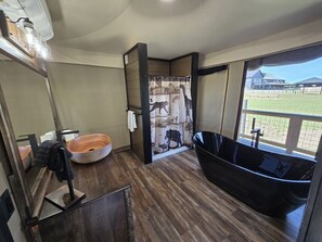 Une salle de bain avec un plancher en bois, un lavabo rond, une baignoire noire et un rideau de douche orné d’un motif représentant des animaux sauvages.