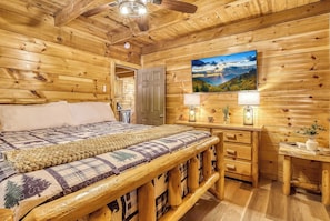 A wooden cabin bedroom with a bed, a desk, a television, and a window with a scenic view. - Starlit Ridge – Hot Tub, Fire Pit, Mountain Views (Sevierville)