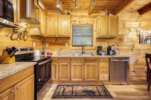 A kitchen with wooden cabinets, a stove, a sink, and a coffee maker. - Starlit Ridge – Hot Tub, Fire Pit, Mountain Views (Sevierville)