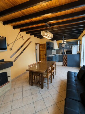 Un comedor con una mesa y sillas de madera, una cocina al fondo y esquíes colgados en la pared.