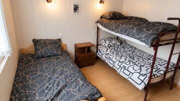 Una habitación con dos literas, una cama individual, un pequeño mesita de noche y dos lámparas fijadas a la pared.