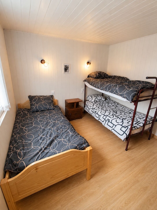 Una habitación con dos literas, una cama individual, un pequeño mesita de noche y dos lámparas fijadas a la pared.