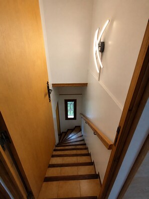 Una escalera de madera con barandilla, un pequeño ventanal en la parte superior e iluminación empotrada en la pared.