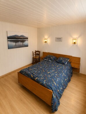 A bedroom with a wooden bed, a chair, a wall-mounted painting, and two wall sconces.