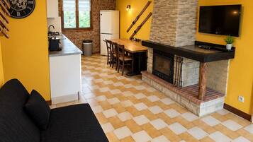 Un espacio habitable moderno con piso a cuadros, un sofá, una zona de comedor, una cocina con chimenea de piedra y un televisor montado.