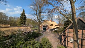 A traditional half-timbered house with a thatched roof, a stone pathway, and a garden with flowering plants.