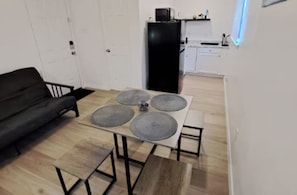 Un espace de vie compact comprenant un canapé, une table à manger avec quatre sets de table, un petit banc et un coin cuisine à l’arrière-plan.