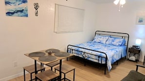 Quarto com cama, mesa e cadeiras, ventilador de teto e janela com persianas.