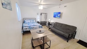 Quarto compacto com cama, sofá, mesa e ventilador de teto.