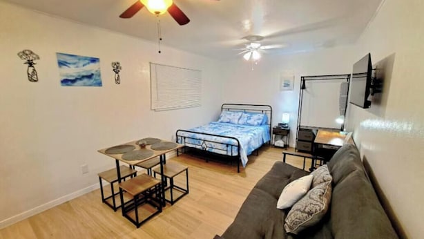 Quarto com cama, escrivaninha, poltrona, sofá, ventilador de teto e janela.