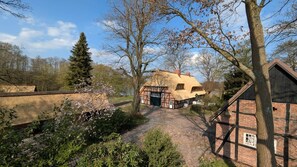 Ein traditionelles Fachwerkhäuschen mit einem Reetdach, einem Kiesweg und einem Garten mit blühenden Pflanzen.