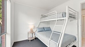Quarto com beliche, uma pequena mesa, abajur, janela e porta.