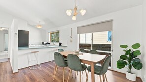 Ett modernt kök med en central köksö, barstolar och en matplats med ett träbord och gröna stolar.