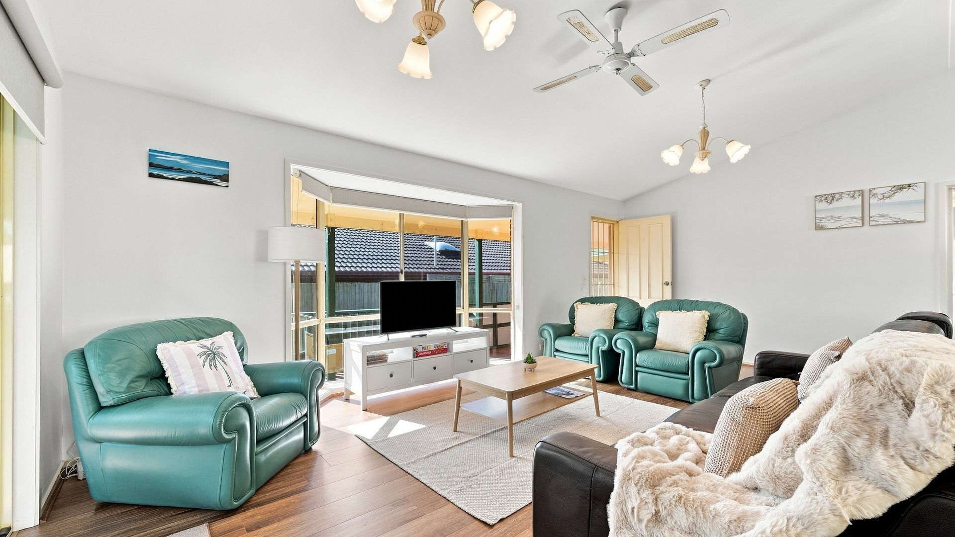 A spacious living room with a large window, a flat-screen TV, and a ceiling fan.