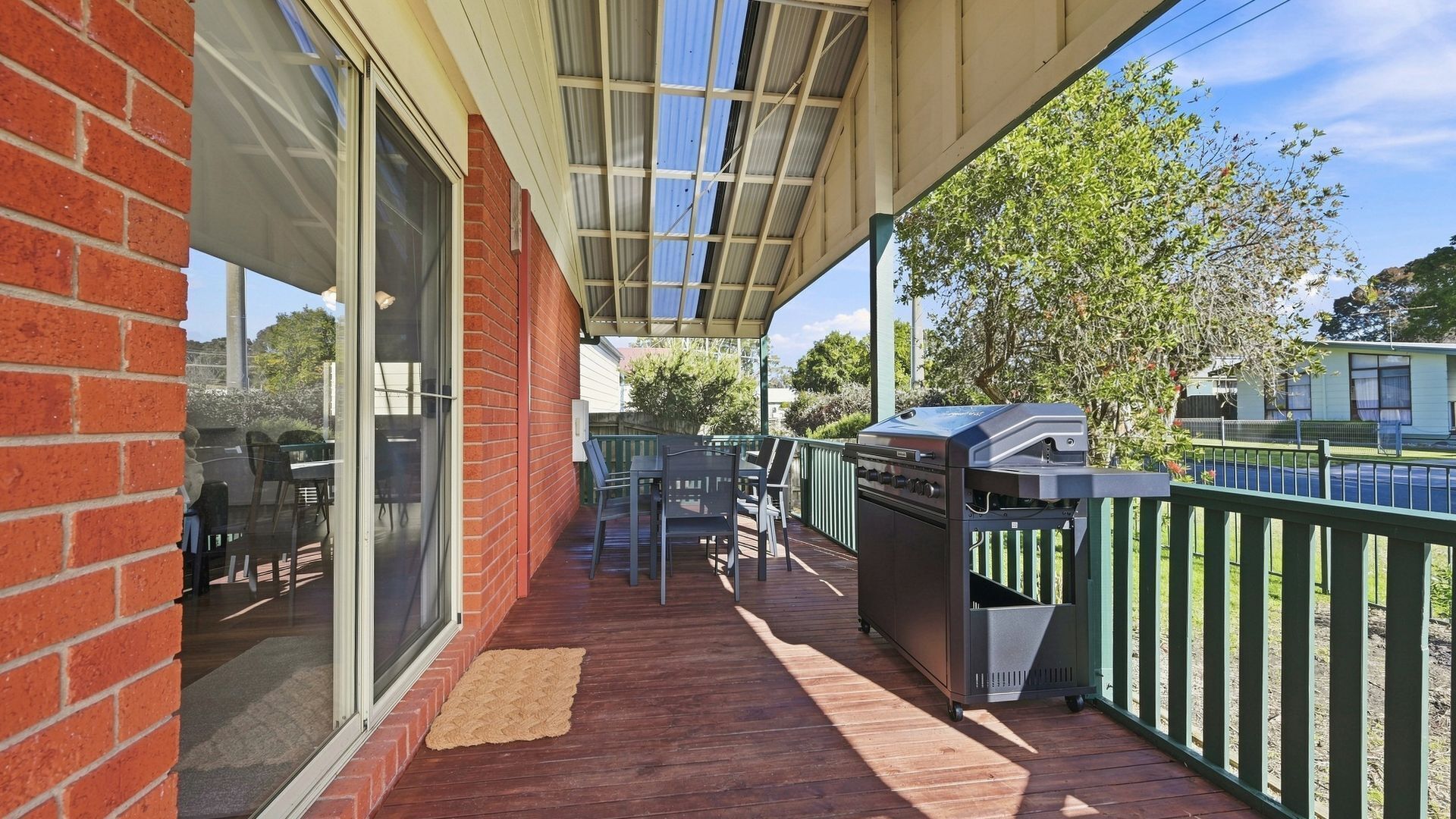 Un espace extérieur abrité comprenant un barbecue, une table avec des chaises et une vue sur une rue résidentielle.