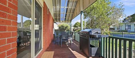 A covered outdoor area with a barbecue grill, a table with chairs, and a view of a residential street.