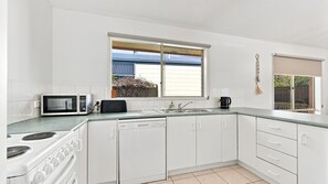 Eine moderne Küche mit weißen Schränken, einer Mikrowelle, einem Herd, einer Spüle und einem Fenster mit Blick auf einen Garten.