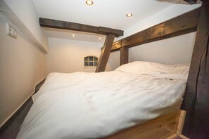 A narrow, sloped room with a bed against the wall, wooden beams, and a small window. - Tüschenbeker Mill - Mühlengarten Apartment (4–5 people) (Groß Sarau)