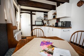 Une cuisine chaleureuse avec des chaises en bois, une table à manger avec des magazines et un four à micro-ondes posé sur le comptoir.