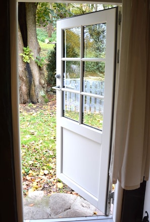 A white door with a glass panel, leading to a garden with a stone path and a wooden fence. - Tüschenbeker Mill - Mühlengarten Apartment (4–5 people) (Groß Sarau)