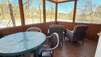 En overdækket terrasse med et glasbord og fletstole, der kigger ud over et boligområde.