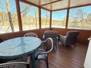 Un patio techado con una mesa de vidrio y sillas de mimbre, con vistas a una zona residencial.