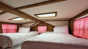 Une chambre avec deux lits, des poutres en bois, des fenêtres de toit et des rideaux à motifs.