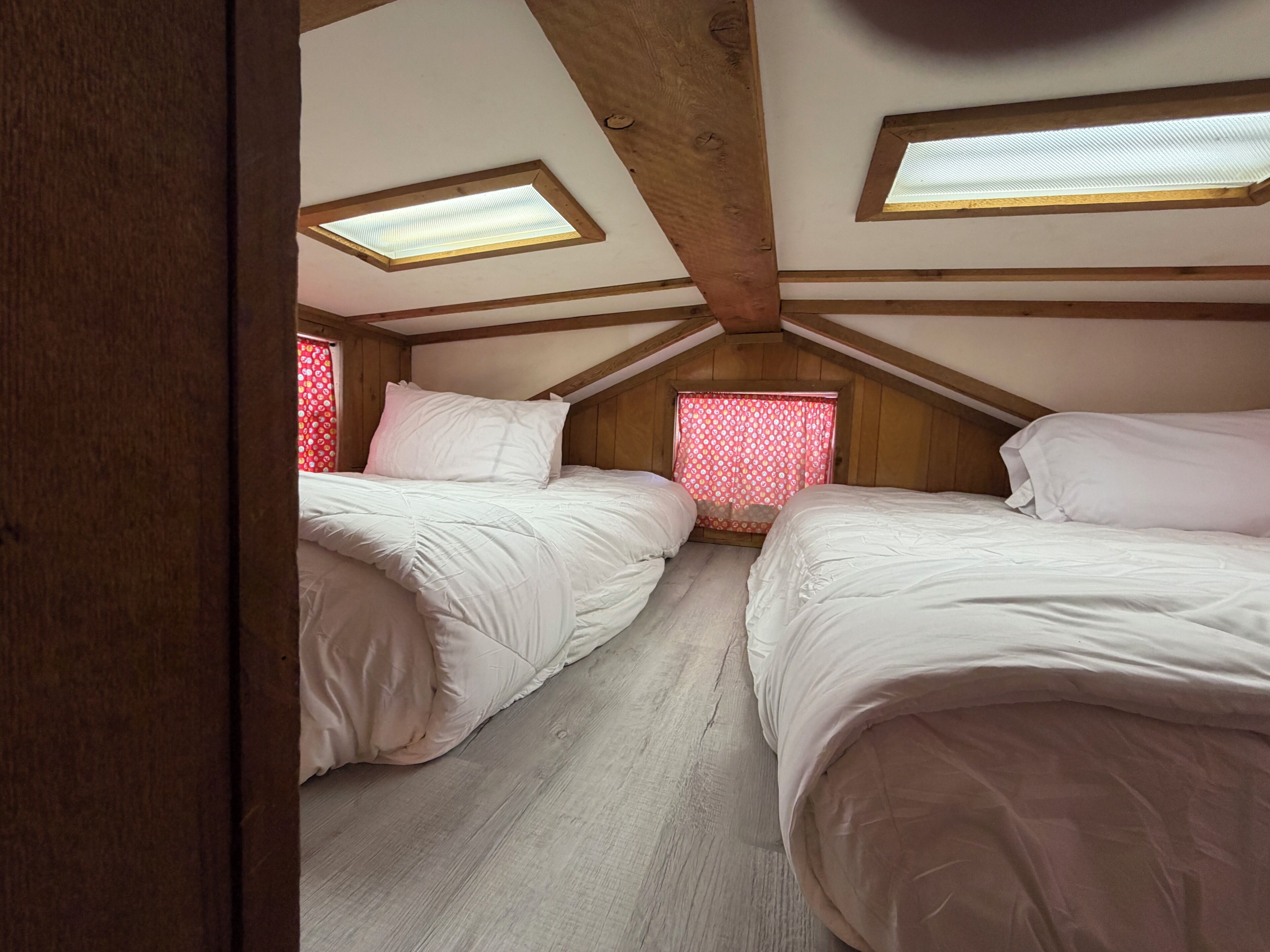 A room with two beds, wooden beams, and skylights.