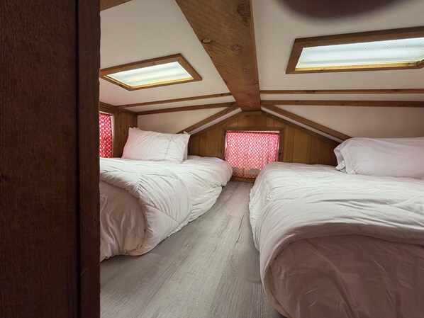 A room with two beds, wooden beams, and skylights.