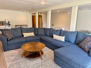 Ein modernes Wohnzimmer mit einer Eckcouch, einem runden Couchtisch und einem gemusterten Teppich.